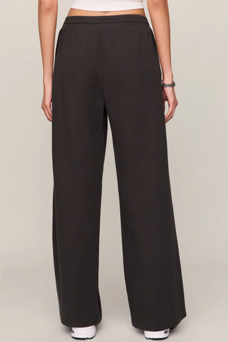 A person shown from the waist down wearing loose, wide-leg black pants against a plain light gray studio background.