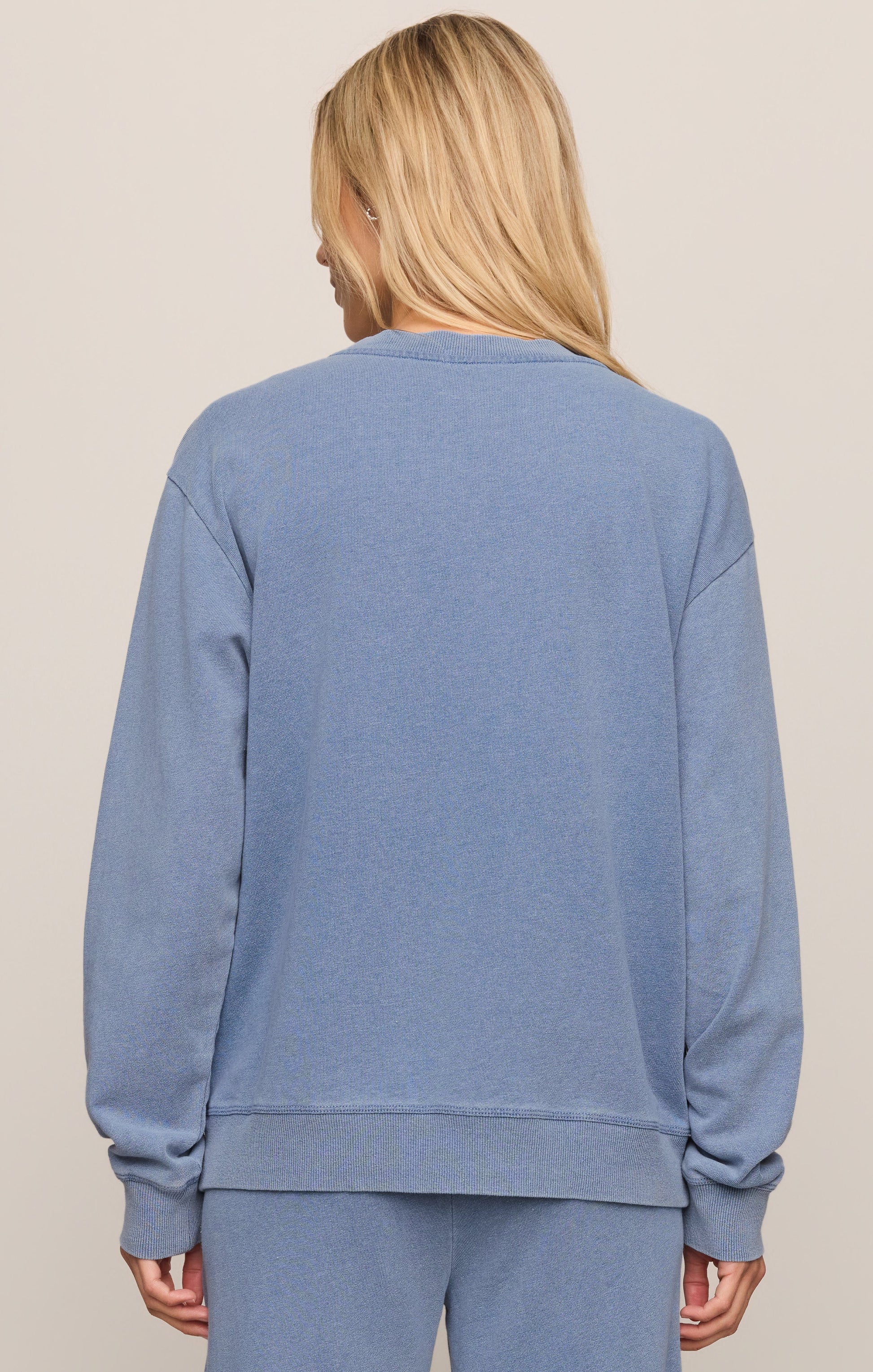 Person wearing a blue sweatshirt and pants on a beige background