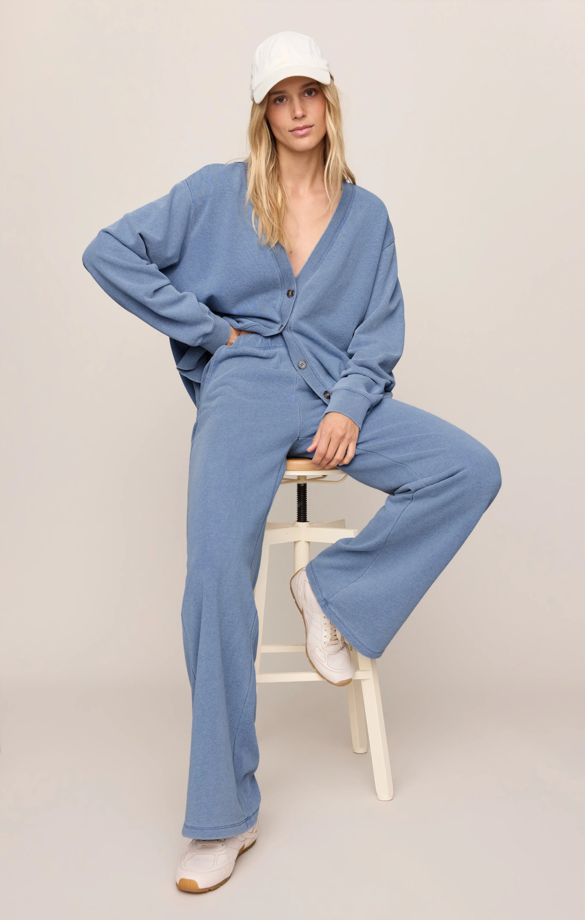Woman wearing a blue outfit sitting on a stool against a plain background